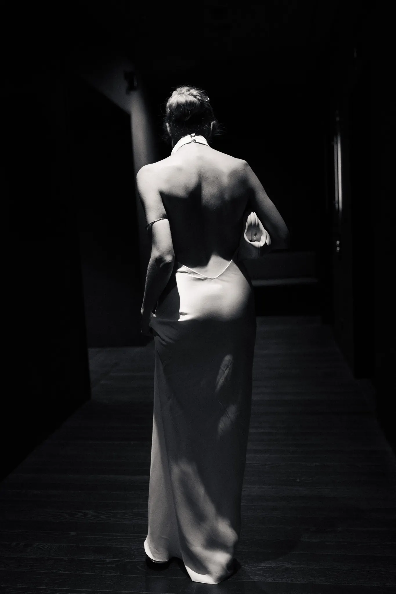 Veronika walking away down a dark corridor, black and white