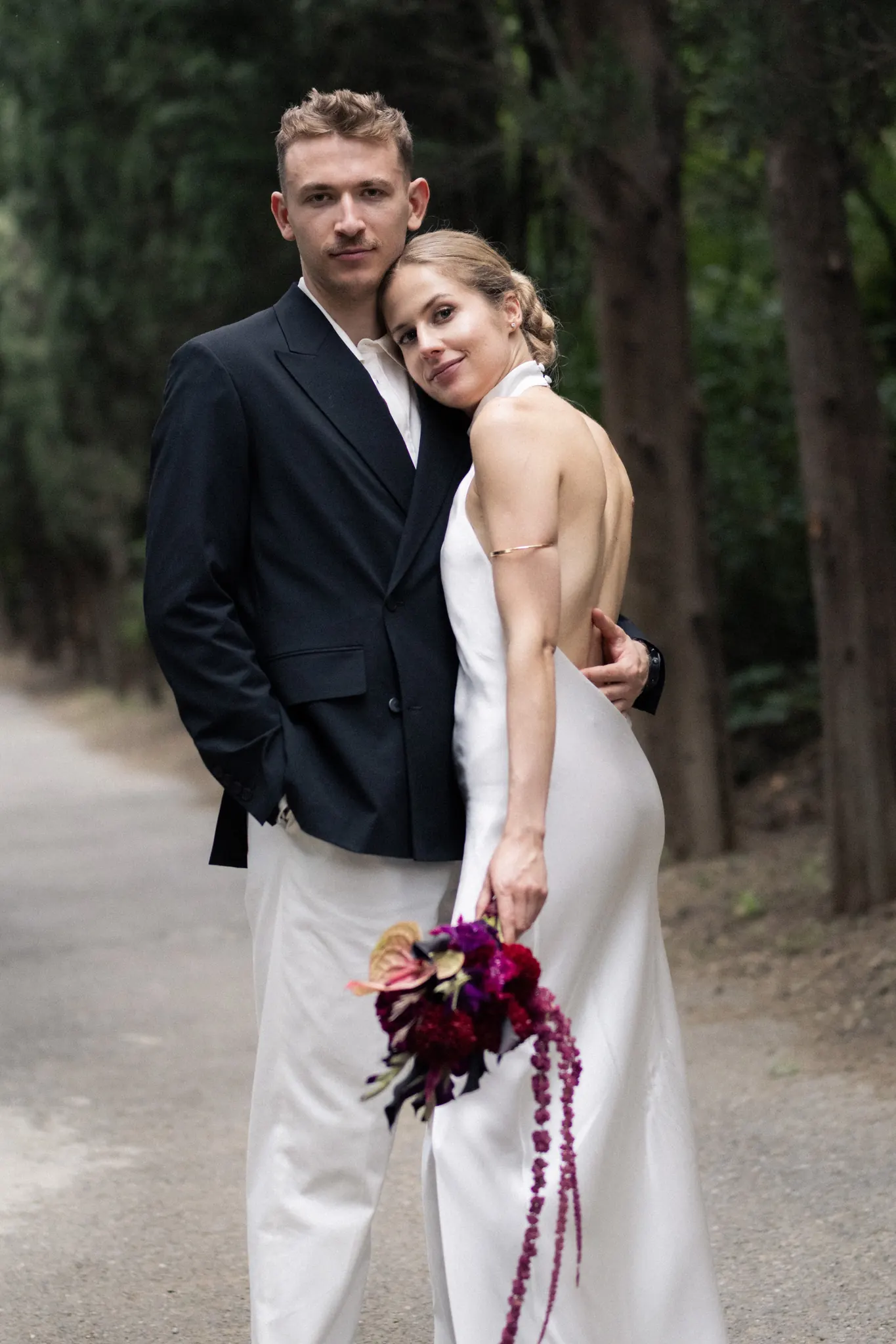 Veronika resting her head on Sasha’s shoulder on a cypress-lined road