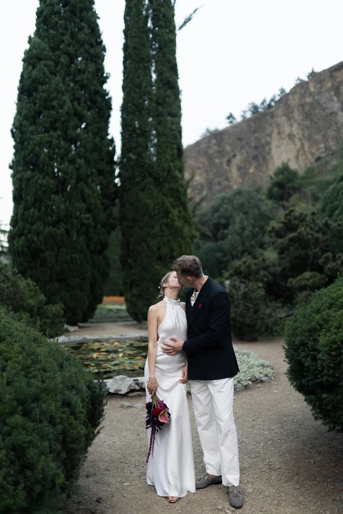 A kiss between tall cypresses beneath a cliff