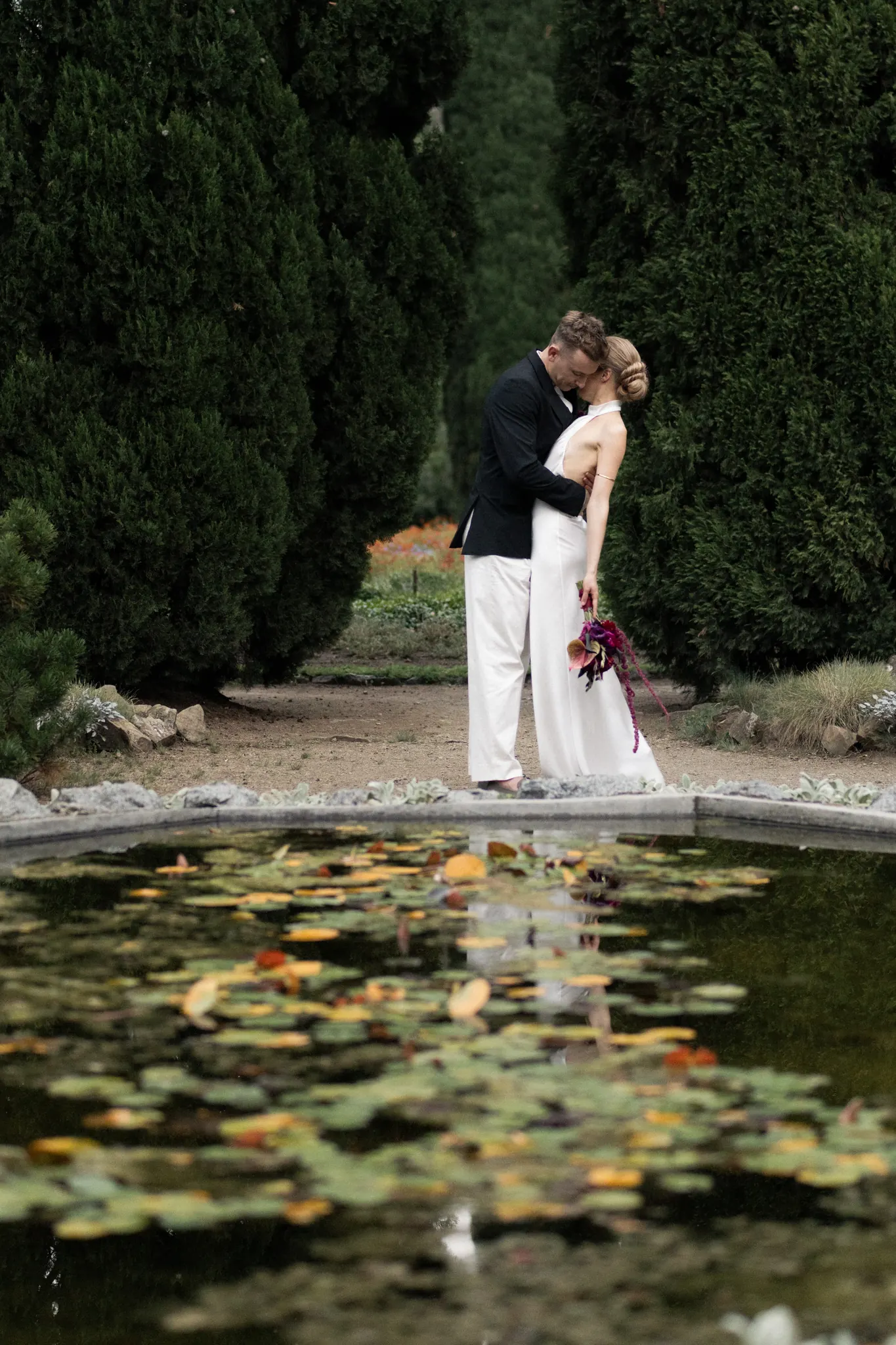 Veronika and Sasha embracing beyond a pond of water lilies