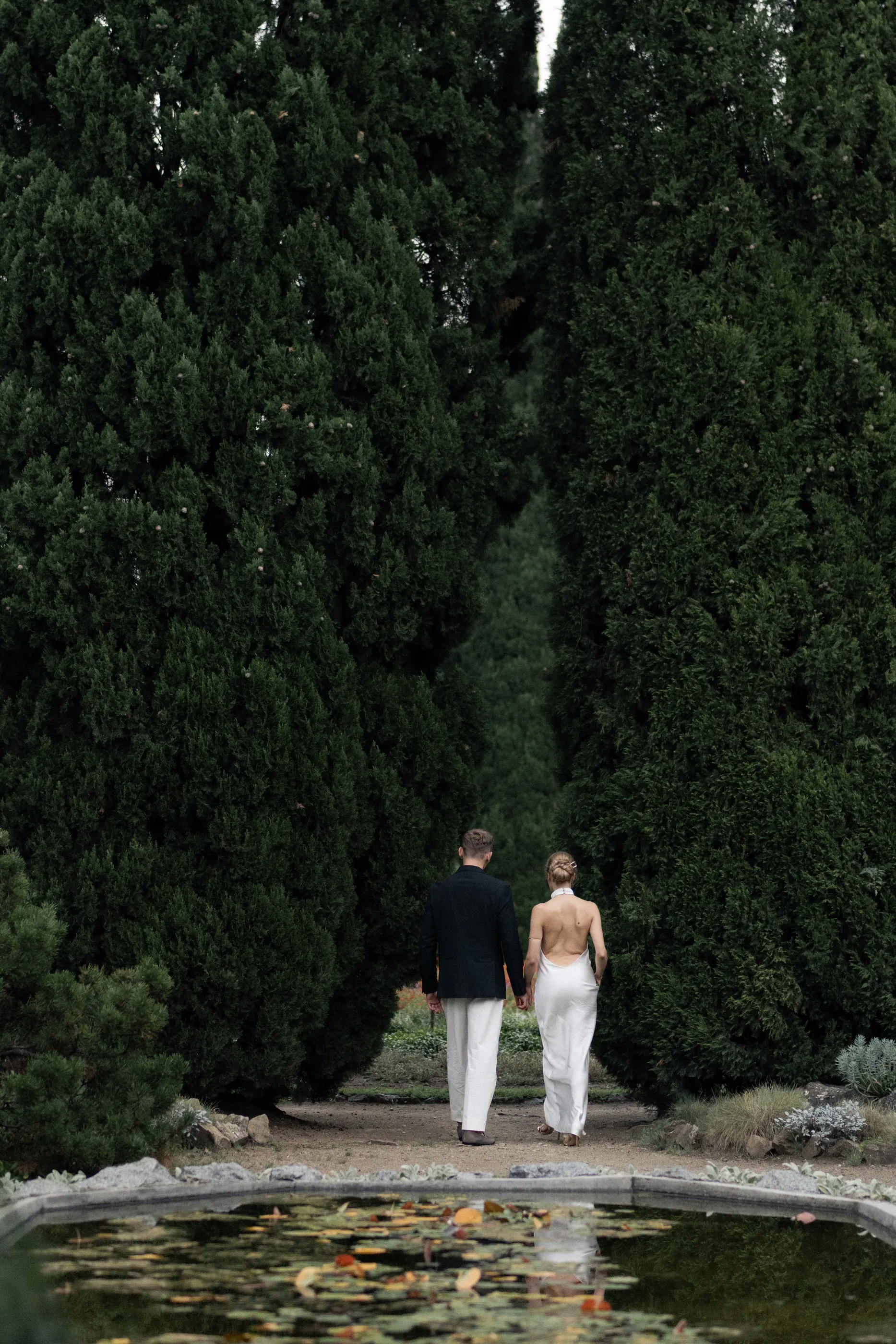Veronika and Sasha walking away between two cypresses