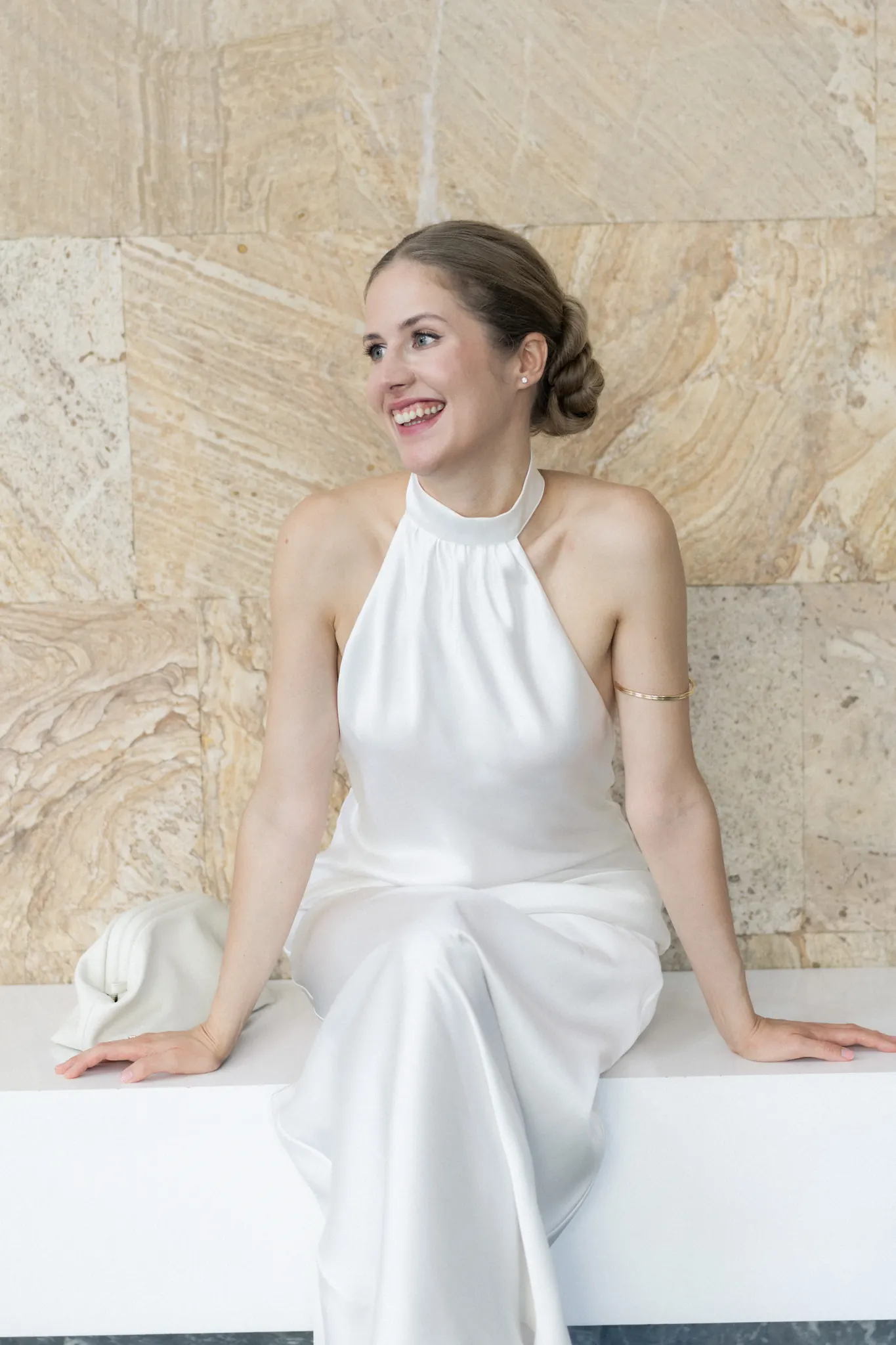 Veronika laughing, seated on a white bench against a stone wall